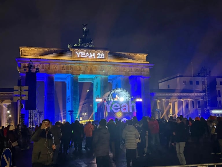 Illuminated Brandenburg Gate at night with blue and yellow lights, YEAH 28 banner, and crowds of people gathered in front